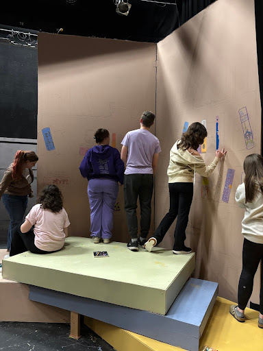 The set crew and cast alike draw the wall of books. 